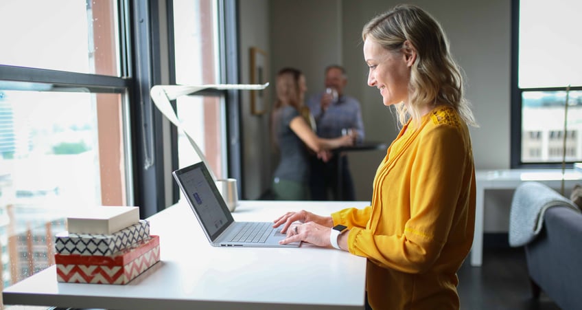 Glad kvinna står vid en dator framför ett fönster