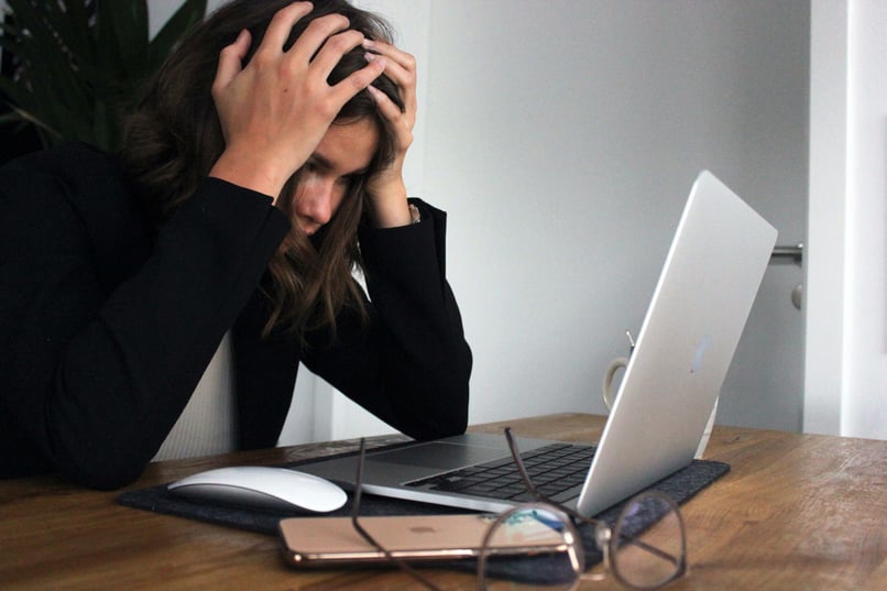 Kvinna sitter framför dator och tar sig för huvudet och ser uppgiven ut