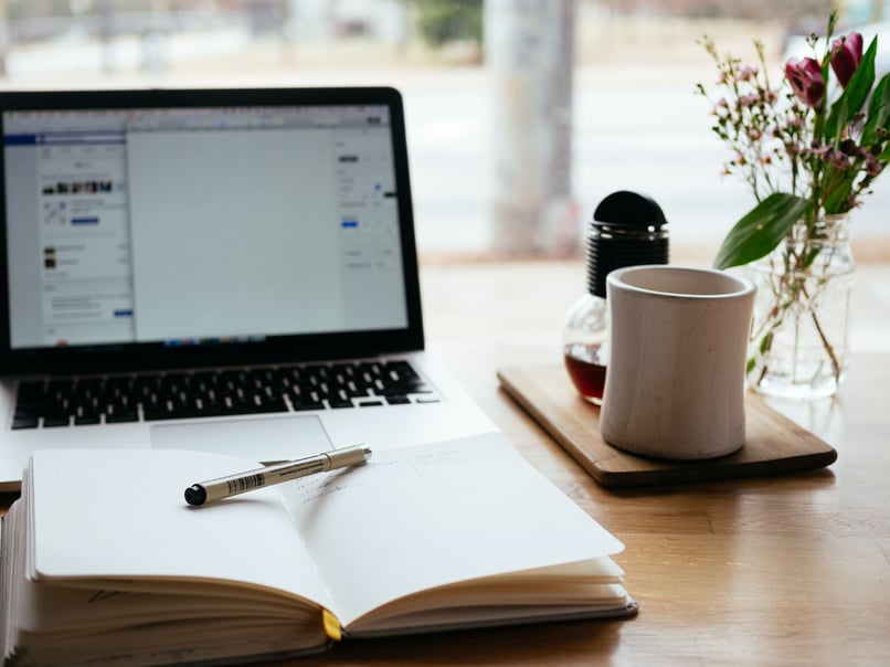 En öppen laptop med, anteckningsblock och kaffe på skrivbordet