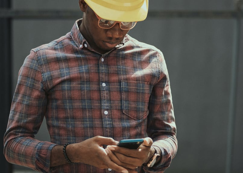 Man_med_mobiltelefon_hård_hatt